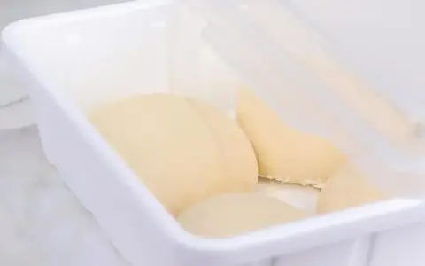 Pâte à pain trop fermenté dans une boîte blanche, prête pour la cuisson.