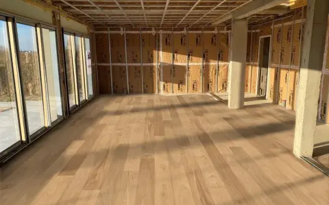 Pose de parquet clair dans une pièce en construction, le sens des lames semble agrandir l'espace.