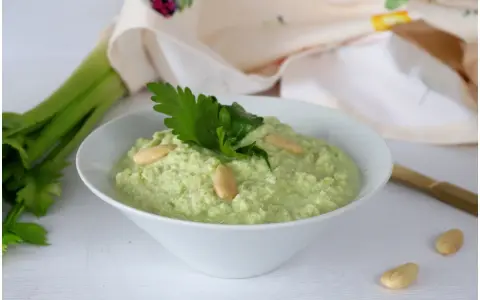 Pesto di sedano fresco, guarnito con mandorle e prezzemolo, pronto per essere gustato.