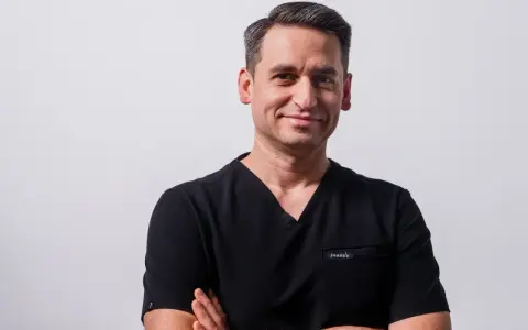 Portret mężczyzny w czarnym scrubie medycznym, ze skrzyżowanymi rękami.