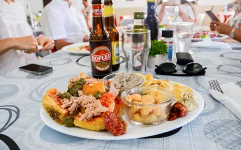Malta jedzenie: talerz z tuńczykiem, kaparami, fasolą i pieczywem, obok piwo i okulary przeciwsłoneczne.