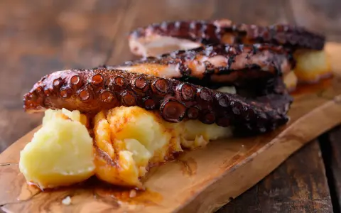 Pulpo tierno con patatas cocidas y espolvoreado con pimentón, servido en tabla de madera.