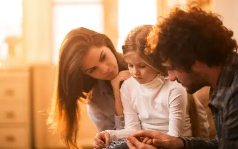 Eltern psychisch kranker Kinder spenden Trost. Ein Vater hält die Hände seiner Tochter, während die Mutter sie zärtlich berührt.