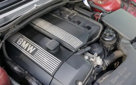 Silniki BMW E46, widok z góry na czarną pokrywę z napisem BMW i srebrnymi paskami. Widać też elementy układu dolotowego i zbiorniczek płynu.