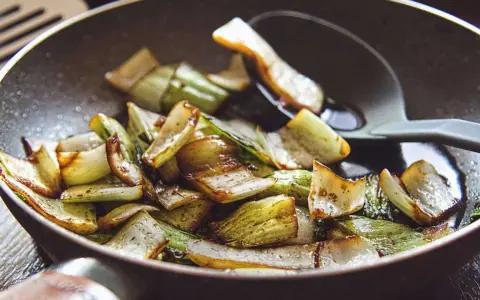 Gebratener Mangold und Pak Choi in einer Pfanne, leicht karamellisiert und mit einem Löffel serviert.