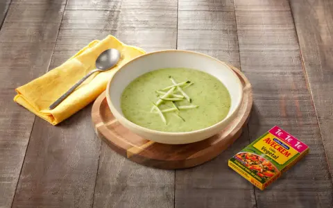 Crema de calabacín para niños, servida en un cuenco blanco sobre tabla de madera. Al lado, un paquete de caldo vegetal Avecrem.