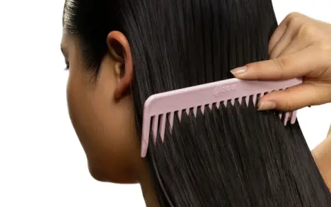 Une main peigne des cheveux noirs et brillants avec un peigne rose. Le peigne est large et espacé, idéal pour démêler les cheveux sans les casser, évitant ainsi les cheveux emmêlés cause.