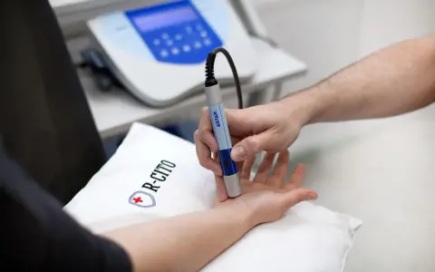 Fizjoterapeuta wykonuje zabieg laserem na dłoni pacjenta.