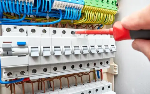 Main électrique avec disjoncteurs. Un tournevis rouge est utilisé pour ajuster une connexion, aidant à comprendre comment savoir quel fusible changer.