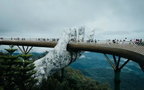 Goldene Brücke in Vietnam, gehalten von einer riesigen Steinhands. Touristen spazieren über die Brücke, die sich durch üppige grüne Berge schlängelt.