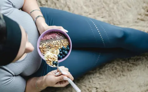 En kvinna äter en näringsrik skål med granola, bär och banan. En bra frukost kan bidra till att uppnå rekommenderat intag av hur mycket protein per dag kvinna.