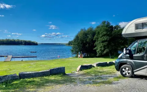 Husbil vid en sjö med brygga, perfekt för fricamping Sverige. Blå himmel och grönska.