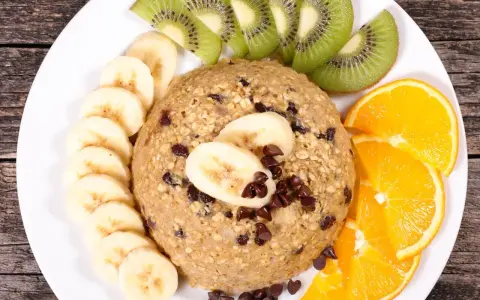 Un délicieux bowl cake flocon d'avoine, garni de rondelles de banane, de tranches de kiwi et d'orange, parsemé de pépites de chocolat.