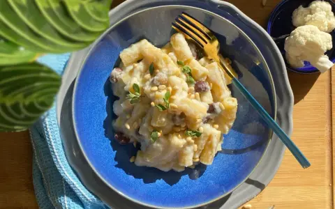Piatto di pasta con cavolfiore cremoso, guarnito con pinoli e erbe aromatiche. Un primo piatto gustoso e leggero.