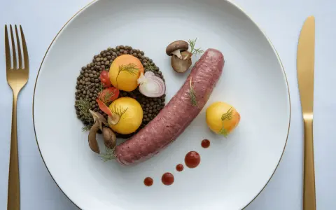 Une saucisse de Toulouse savoureuse, accompagnée de lentilles, de tomates cerises, de champignons et de petites pommes de terre dorées.
