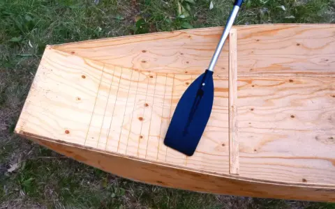 Bateau en contreplaqué brut, prêt pour la résine époxy. Une pagaie noire repose à l'intérieur.