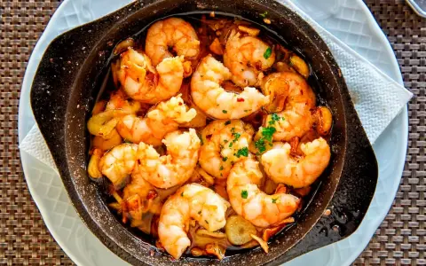 Un plato humeante de langostinos al ajillo, jugosos y dorados, nadando en aceite de oliva con ajo y perejil. ¡Un manjar irresistible!
