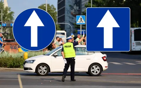 Policjant kieruje ruchem przy znakach droga jednokierunkowa. Biała Skoda czeka na sygnał.