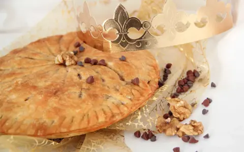 Une galette des rois pépite de chocolat dorée, parsemée de pépites de chocolat et de noix, sous une couronne royale.