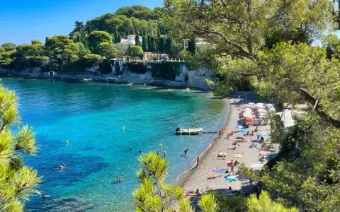 Plage idyllique à Antibes, eaux turquoise, pins parasols et villas sur la falaise. Parfait pour visiter Antibes et se détendre.