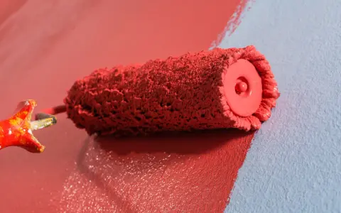 Rodillo de pintura roja creando burbujas al aplicarla sobre pared azul.