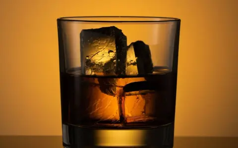 Ein Glas mit **whiskey neat**, zwei große Eiswürfel darin, beleuchtet von warmem Licht.