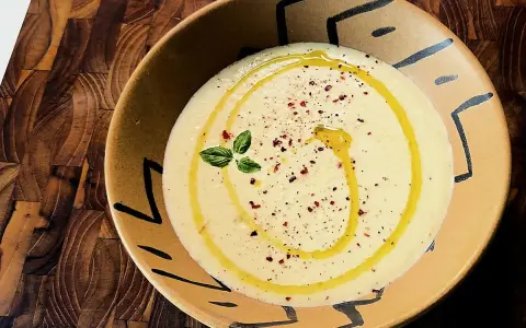Gazpacho de calabacín cremoso, con un hilo de aceite de oliva, pimentón y una ramita de albahaca, servido en un cuenco artesanal.