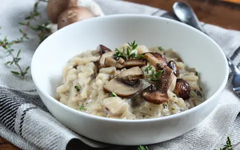 Aksamitne risotto z pieczarkami, udekorowane świeżym tymiankiem, w białej misce na lnianej serwetce.