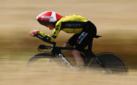 A cyclist in a yellow and black suit, helmet, and aero bars races during the Dauphine cycling event, blurring past the camera.