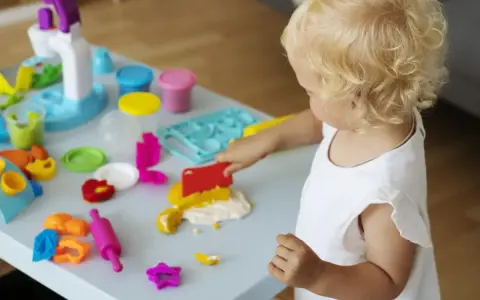 Małe dziecko z blond włosami bawi się masą plastyczną, wspierając swój rozwój sensoryczny.