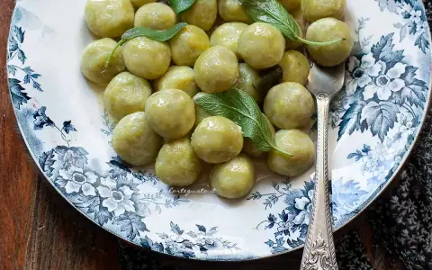 Gnocchi di zucchine morbidi e profumati, guarniti con foglie di salvia fresca su un piatto decorato.