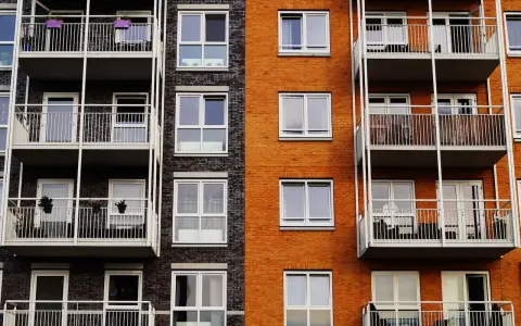 Fachada de edificio moderno con ladrillo naranja y oscuro, balcones blancos y ventanas. Un proyecto de reforma fachada casa que realza su estética.