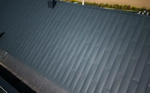 Nowoczesny dach pokryty ciemnoszarą blachą na rąbek, z widocznym kominem i oknem dachowym.
