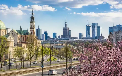 Majówka w Warszawie: zabytkowy kościół i nowoczesne wieżowce na tle kwitnącej wiśni.