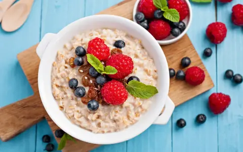Un tazón de avena con frambuesas, arándanos y pasas. Descubre los beneficios de la avena por la noche para un descanso reparador.