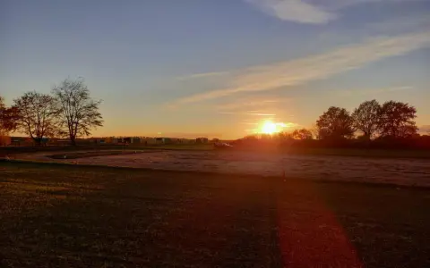 Sonnenuntergang über einem Feld mit Bäumen und einem Auto. "Seid stille und wisset: Ich bin Gott." (Psalm 46:10)