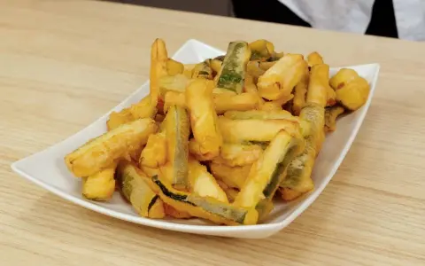 Un piatto bianco pieno di zucchine in pastella dorate e croccanti, pronte per essere gustate.