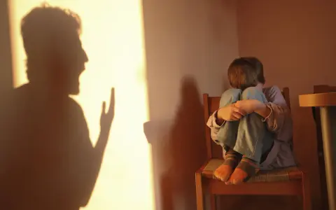 Cień krzyczącego dorosłego rzuca się na ścianę, podczas gdy dziecko skulone na krześle czeka na bicie po pupie.