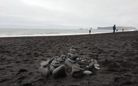 Kamienne stosy na czarnej plaży Islandii, z widokiem na ocean i skaliste wybrzeże.