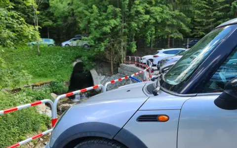 Samochody zaparkowane w dolinie małej łąki, przy strumieniu. W tle las i zielone wzgórza.