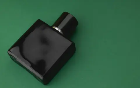 Czarna, elegancka butelka perfum z nutą wetiwery na zielonym tle.