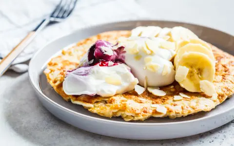 Puszysty omlet z jogurtem, jagodami, bananem i płatkami migdałów. Idealny przepis na zdrowy omlet na śniadanie.