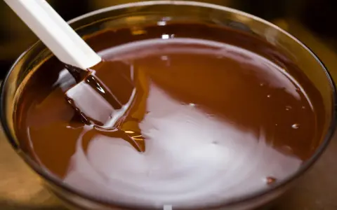 Spatule blanche remuant du chocolat fondu dans un bol en verre. Le chocolat est lisse et brillant, prêt à être utilisé pour une recette.