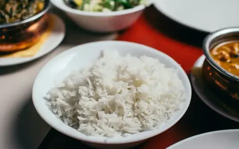 Biały ryż, źródło węglowodanów, w misce obok indyjskiego curry i sałatki.