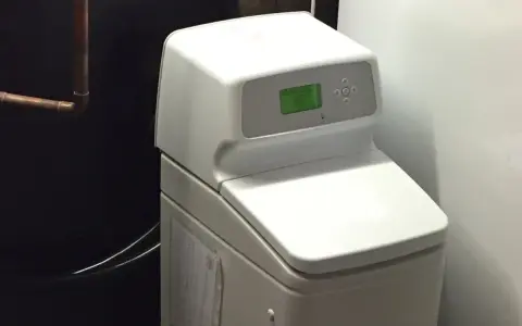 Adoucisseur d'eau blanc avec écran vert, un avantage pour une eau plus douce et une maison protégée.