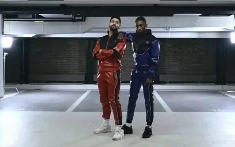 Two gay men in matching red and blue sportswear pose in a parking garage.