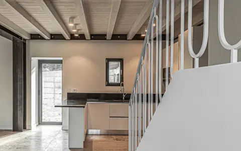 Interno moderno con travi a vista in legno, illuminazione led soffusa e una scala bianca.