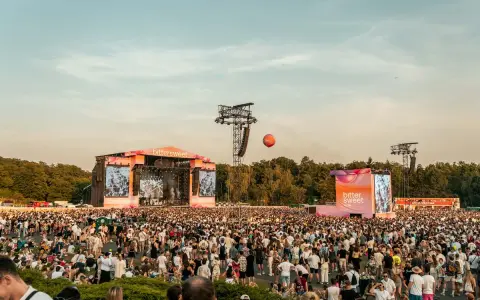Tłum ludzi na festiwalu bittersweet, dwie sceny, ekrany z grafikami i pomarańczowy balon na niebie.