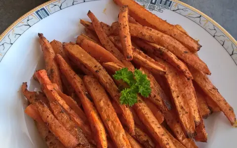Stos pieczonych frytek z marchewki z natką pietruszki na talerzu.