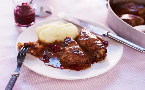 Kåldolmar recept: två saftiga kåldolmar med potatismos och lingonsylt, serverade med en mustig sås.
